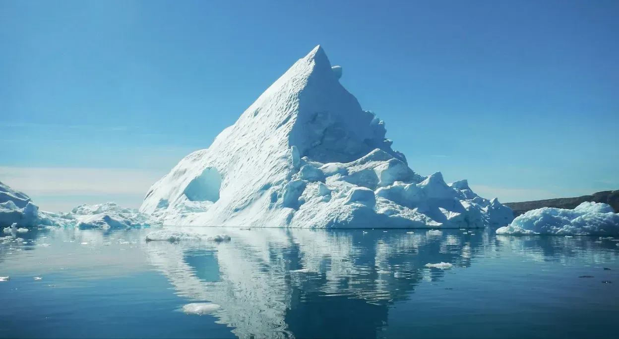 Iceberg floating in calm blue water, reflected on the surface