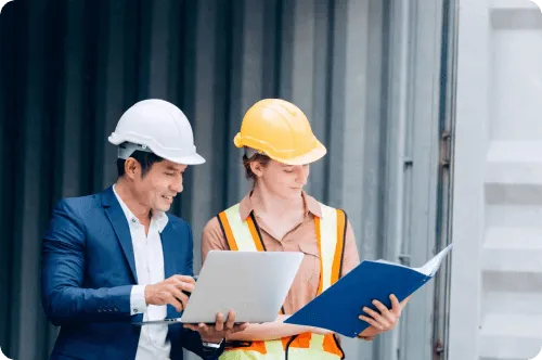 Two logistics staff in hard hats reviewing shipping documents beside a container